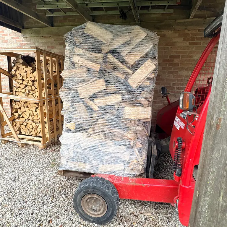 Palette de bûches déposée sous le carport, à côté du bois déjà rangé